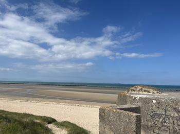 German pill box on right side of photograph on the sands of Normandy beach on a sunny day.