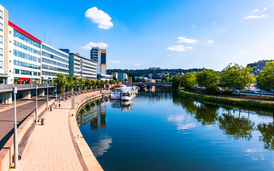 This vibrant photo showcases the modern riverside promenade along the Saar River in Saarbrücken, Germany. Featuring sleek contemporary architecture, tree-lined walkways, and docked boats, the scene highlights the city’s perfect blend of urban living and natural beauty. With its inviting atmosphere, this area is ideal for a leisurely stroll, riverside dining, or exploring the charm of Saarbrücken’s waterfront.