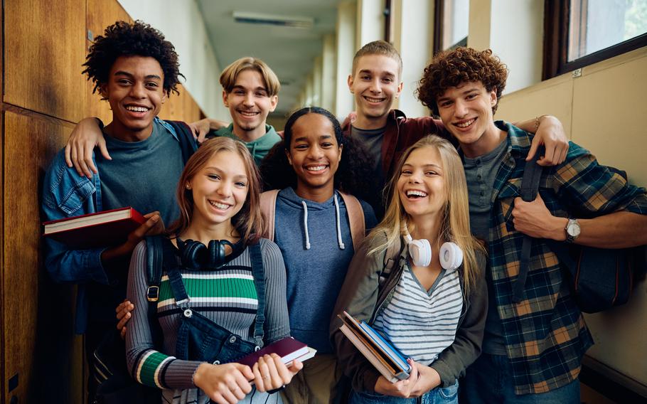 A group of seven teenagers smile at the camera with their arms around each other. 