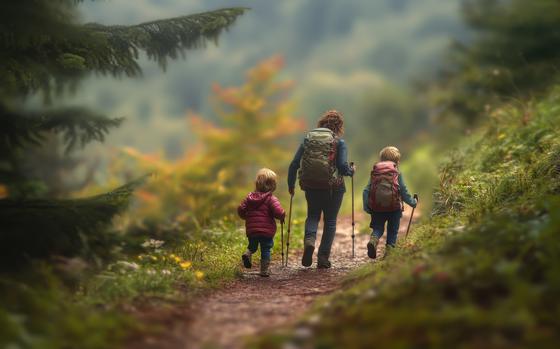 A woman and two children walk along a wooded path surrounded by colorful autumn foliage.