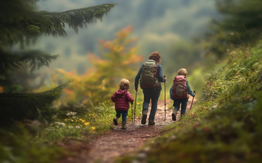 A woman and two children walk along a wooded path surrounded by colorful autumn foliage.