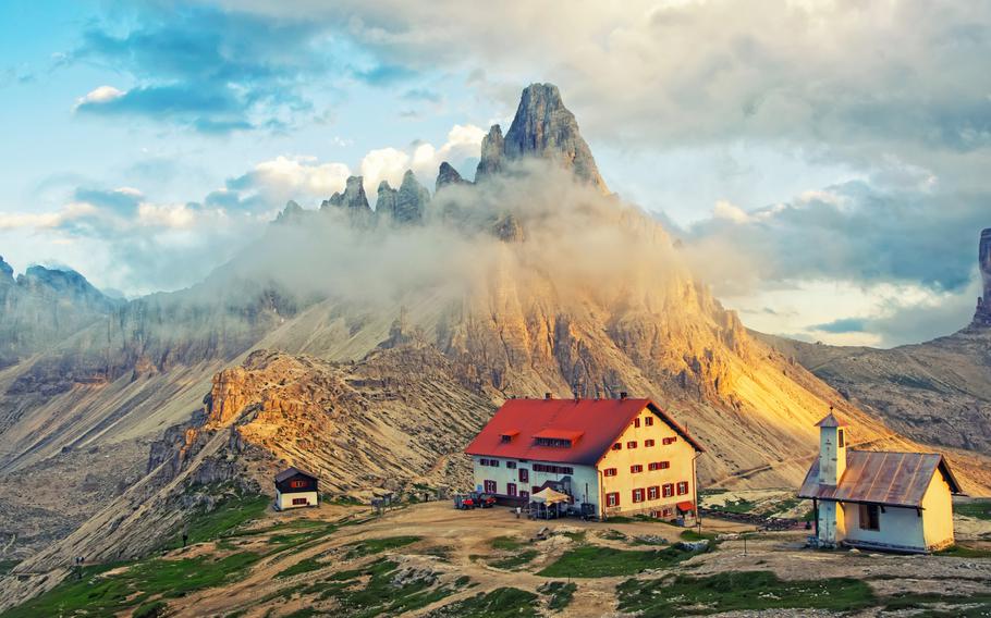 Image of a mountain chalet on a high plateau beneath jagged rocky mountains.