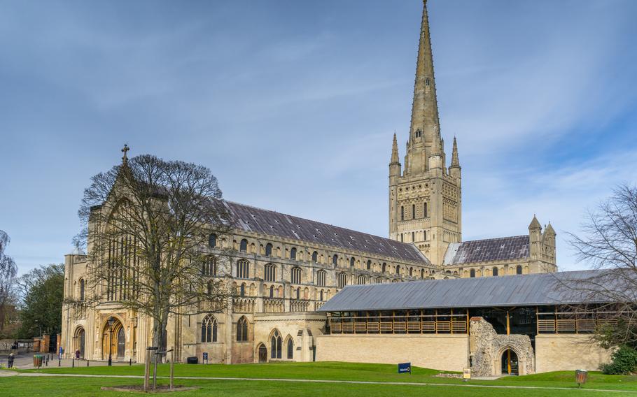 A close up of Norwich Cathedral. The grass is green and the church is large with elements of gothic spirals and architecture.