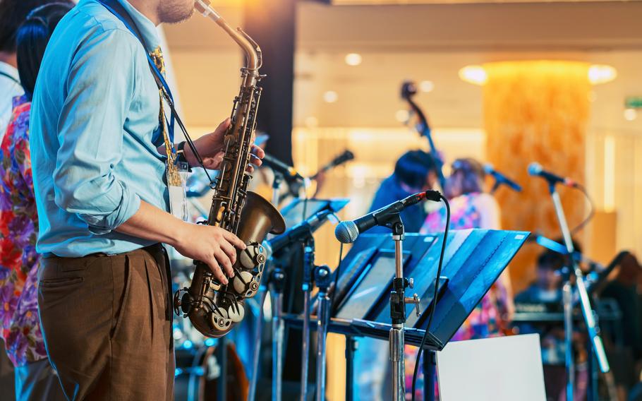 Musician playing saxophone on blurred background. Man with friends blow saxophone with the band for performance. 