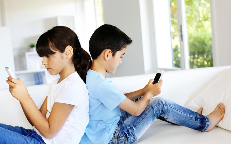 Kids sitting back-to-back playing on smartphones