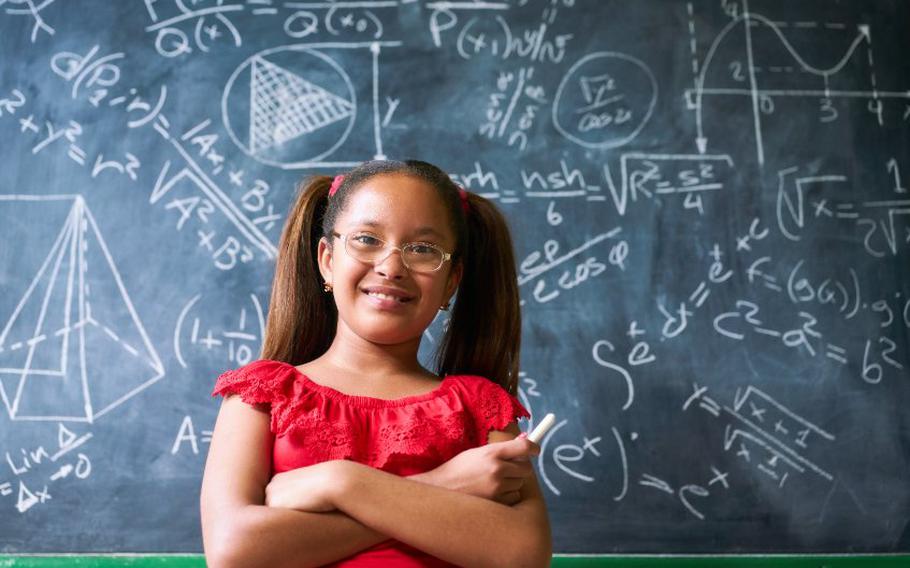 Child smiling and standing in front of chalkboard.