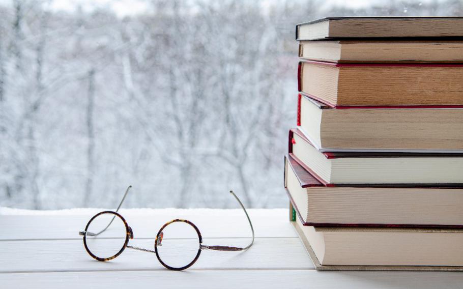 Old multi-colored books and a pair of glasses against the backdrop of the winter forest