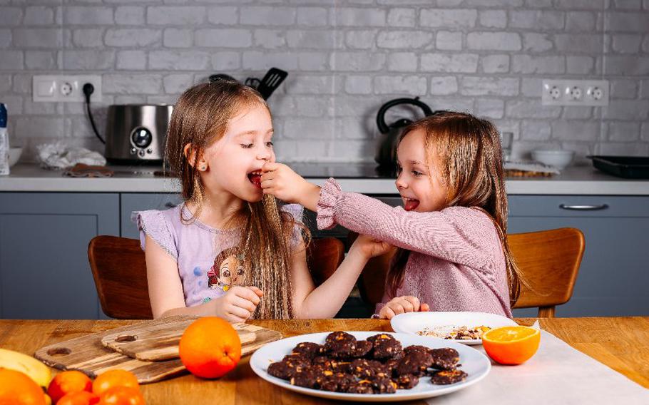 Two kids eating snacks while sitting at table.