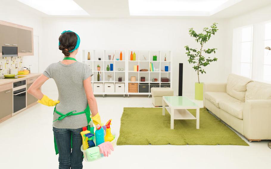 Woman holding cleaning supplies and looking into a room