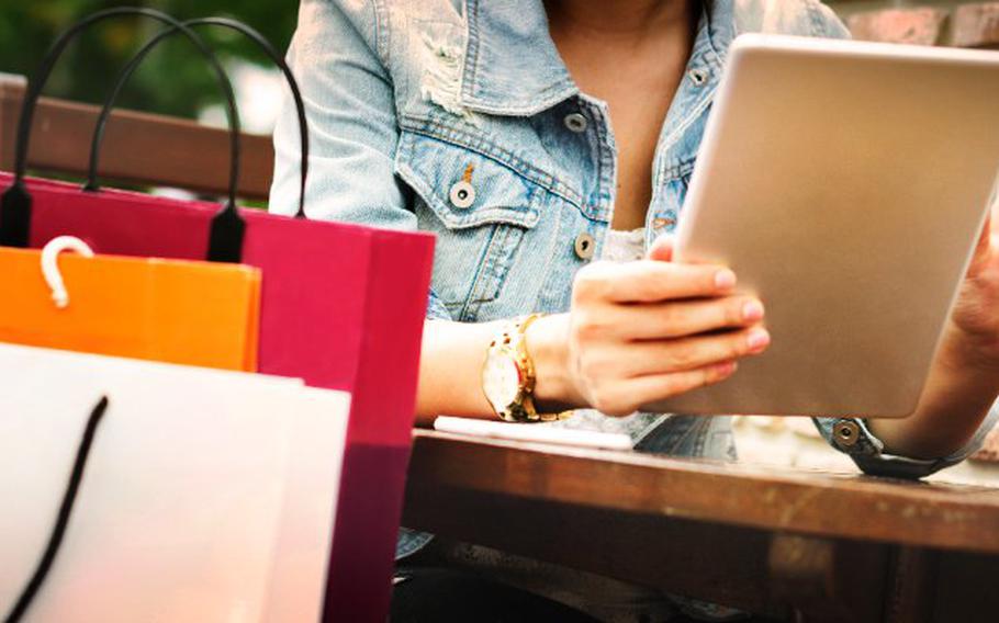 Person scrolling on tablet with three shopping bags in front.