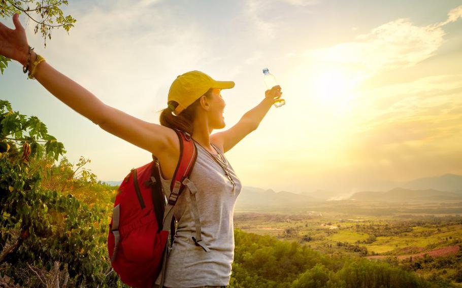 Traveler with backpack and a bottle of water standing on top of the mountain