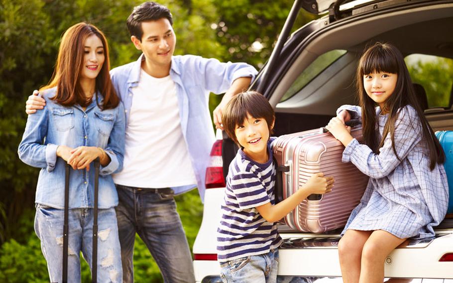 Boy and girl sitting in back of SUV helping to unload luggage with parents standing next to them