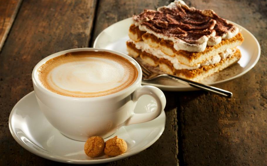 Cup of coffee with piece of cake on wooden table.