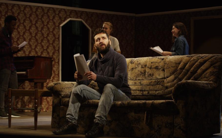 Actor reciting his lines on a sofa while other actors rehearsing in the background