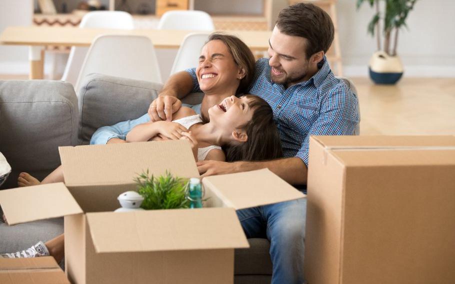 Family sitting on couch smiling and laughing surrounded by moving boxes.