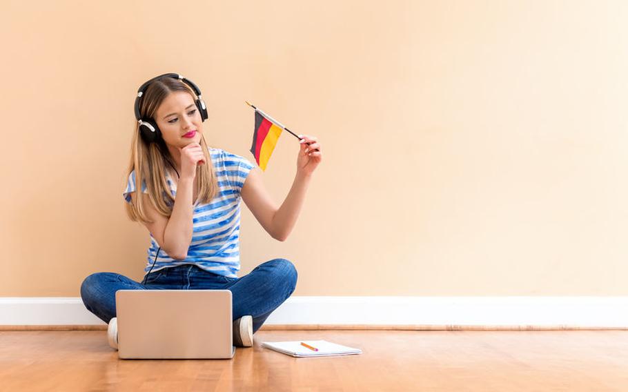 Women sitting on floor wearing headphones holding a German flag in front of a laptop