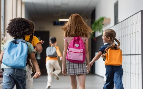 Photo Of Back view of schoolchildren with backpacks walking in corridor of school