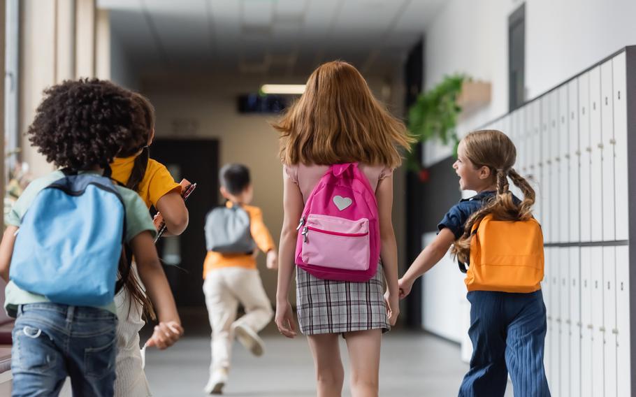 Back view of schoolchildren with backpacks walking in corridor of school