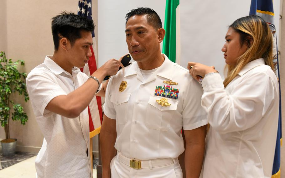 Security Officer Lt. Cmdr. Lamis Alexander's children place his commander shoulder boards in a promotion ceremony at the Naval Support Activity (NSA) Naples' Capodichino Chapel, June 1, 2023. NSA Naples is an operational ashore base that enables U.S., allied, and partner nation forces to be where they are needed, when they are needed to ensure security and stability in the European, African, and Central Command areas of responsibility. (U.S. Navy photo by Aaliyah Essex)